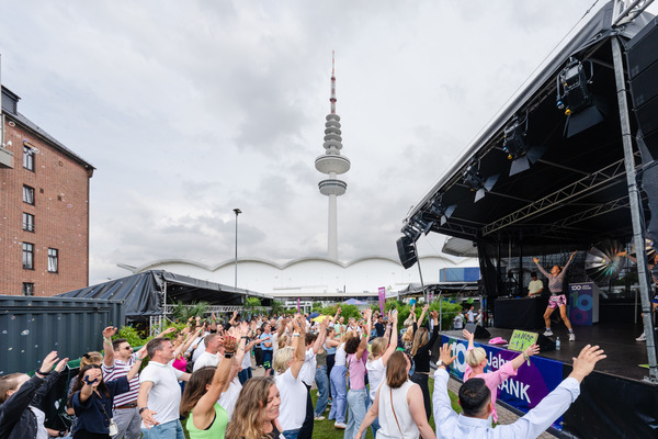 FRANK Mitarbeiter Tanzen vor der Bühne, man sieht das Festivalgelände und den Fernsehturm im Hintergrund